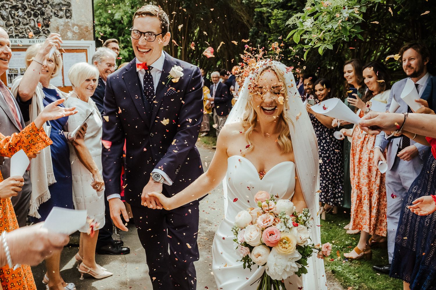 Joyful wedding exit with guests throwing confetti in a sunlit garden setting.