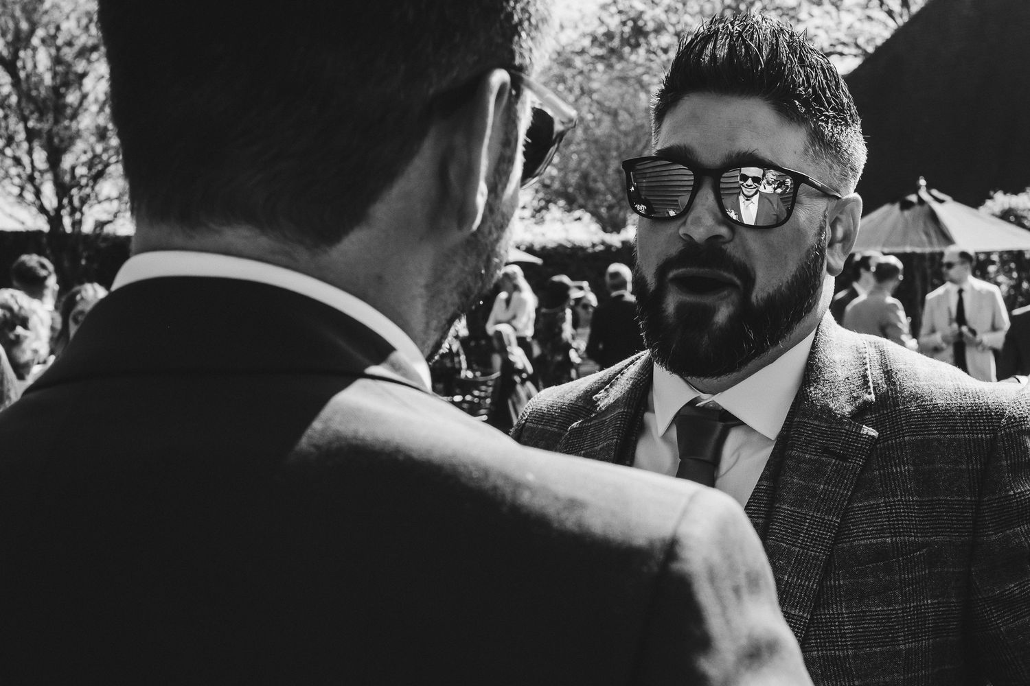 Two men in formal attire having intimate conversation at outdoor wedding.