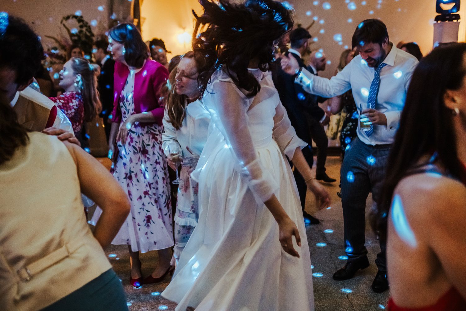 Wedding guests dancing and celebrating on a lively dance floor under decorative lights.