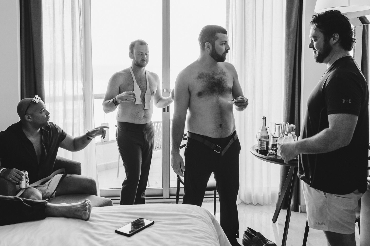 Group of friends hanging out and drinking in a bright hotel room.