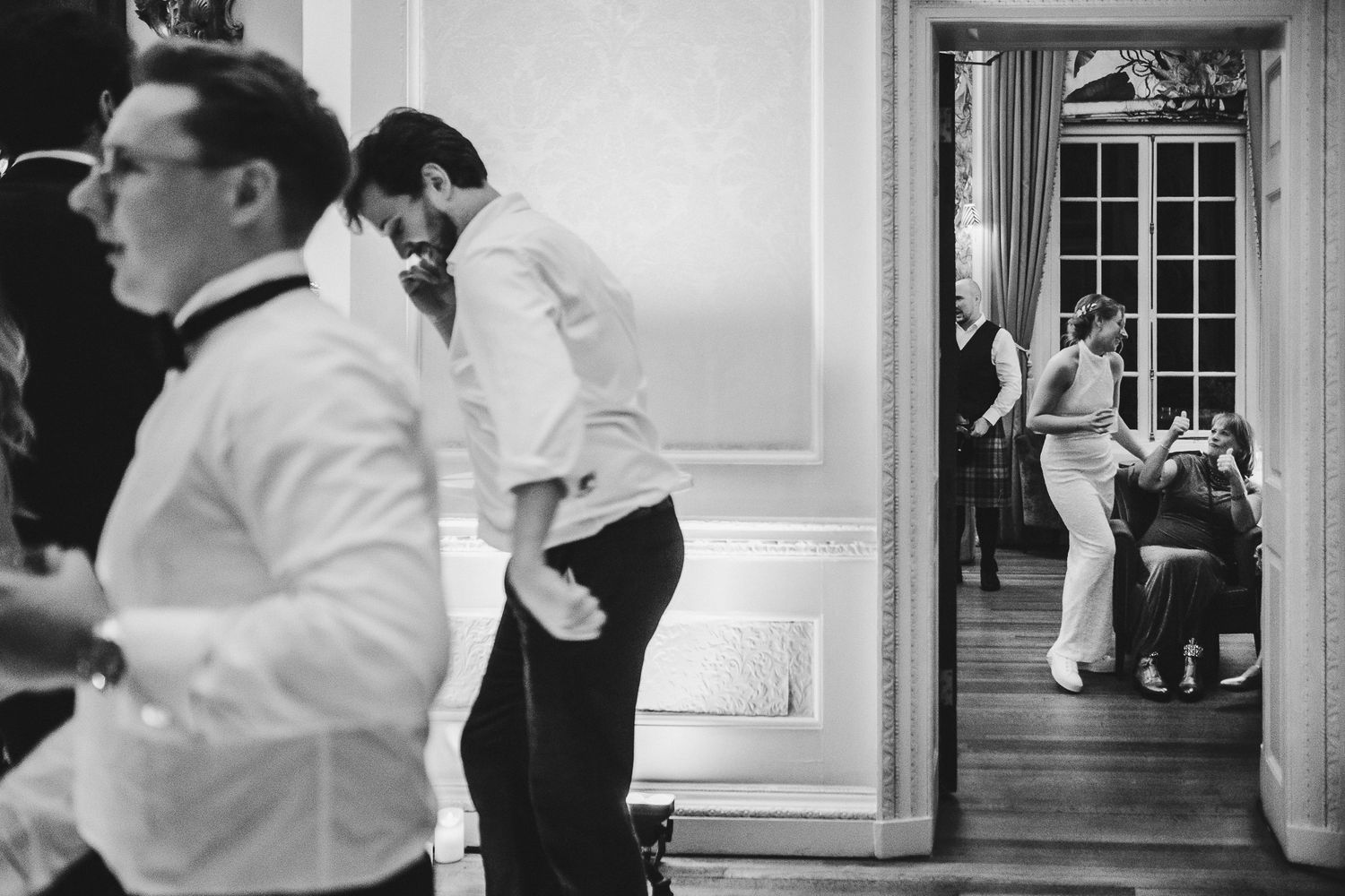 Black and white reception photo showing multiple rooms with guests mingling in formal attire.
