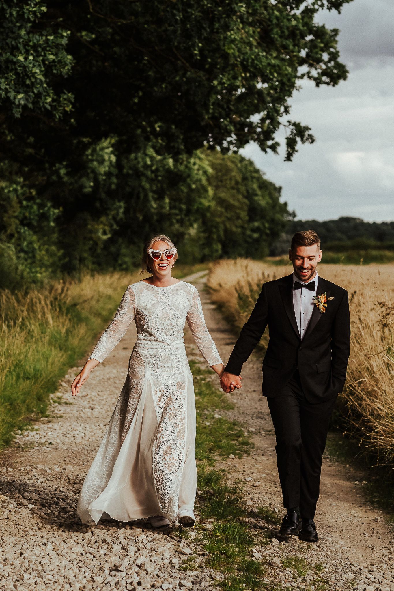 Newlyweds walking down a country path with the bride in a lace dress and groom in classic tuxedo.