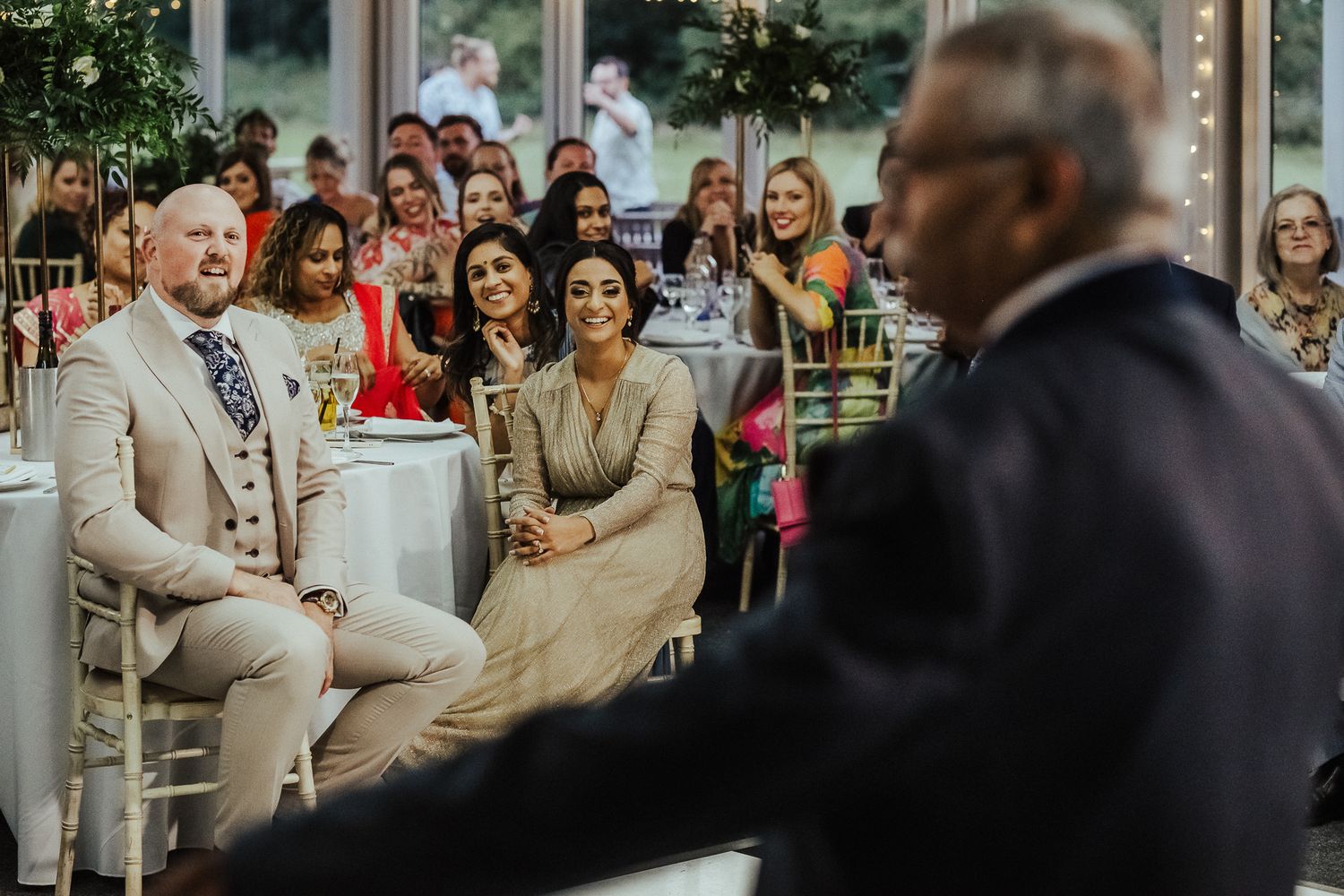Wedding guests smile and laugh during an emotional celebration at an elegant indoor venue.