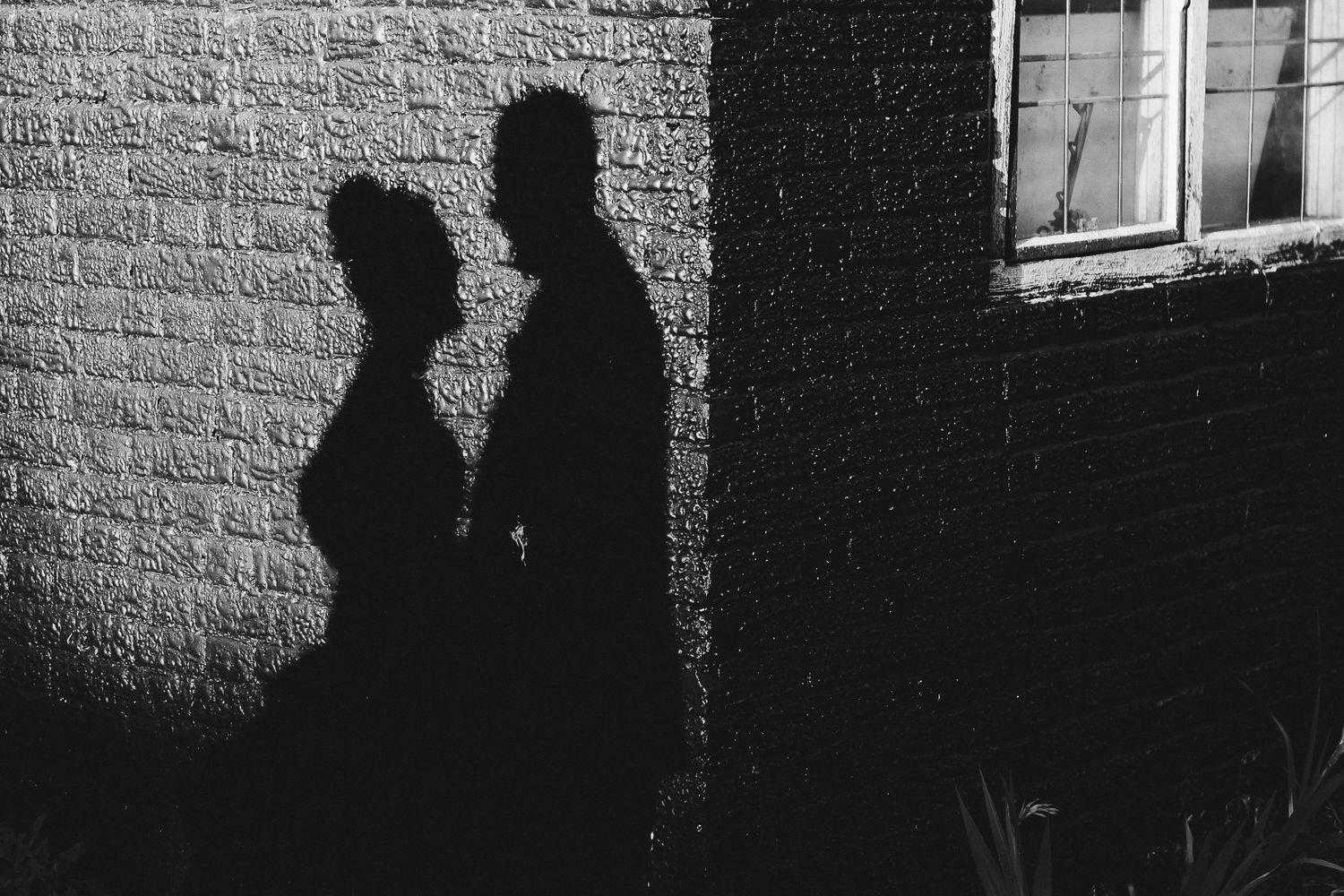Dramatic black and white silhouette of two figures against a brick wall.
