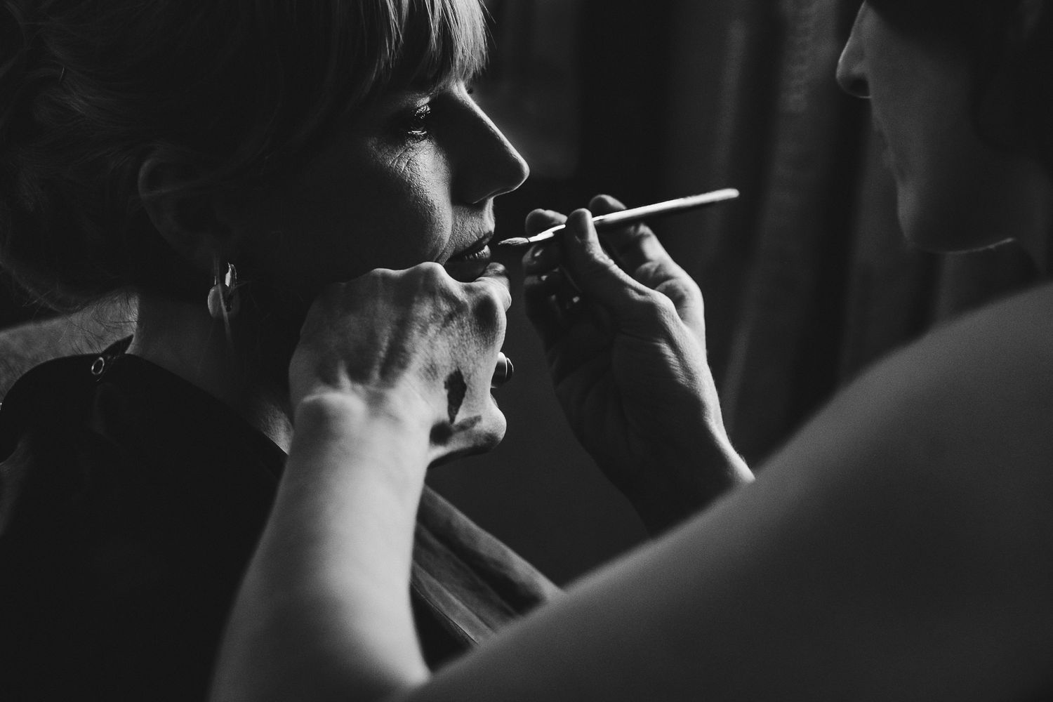 Black and white image of someone having makeup applied with a brush in dramatic lighting.