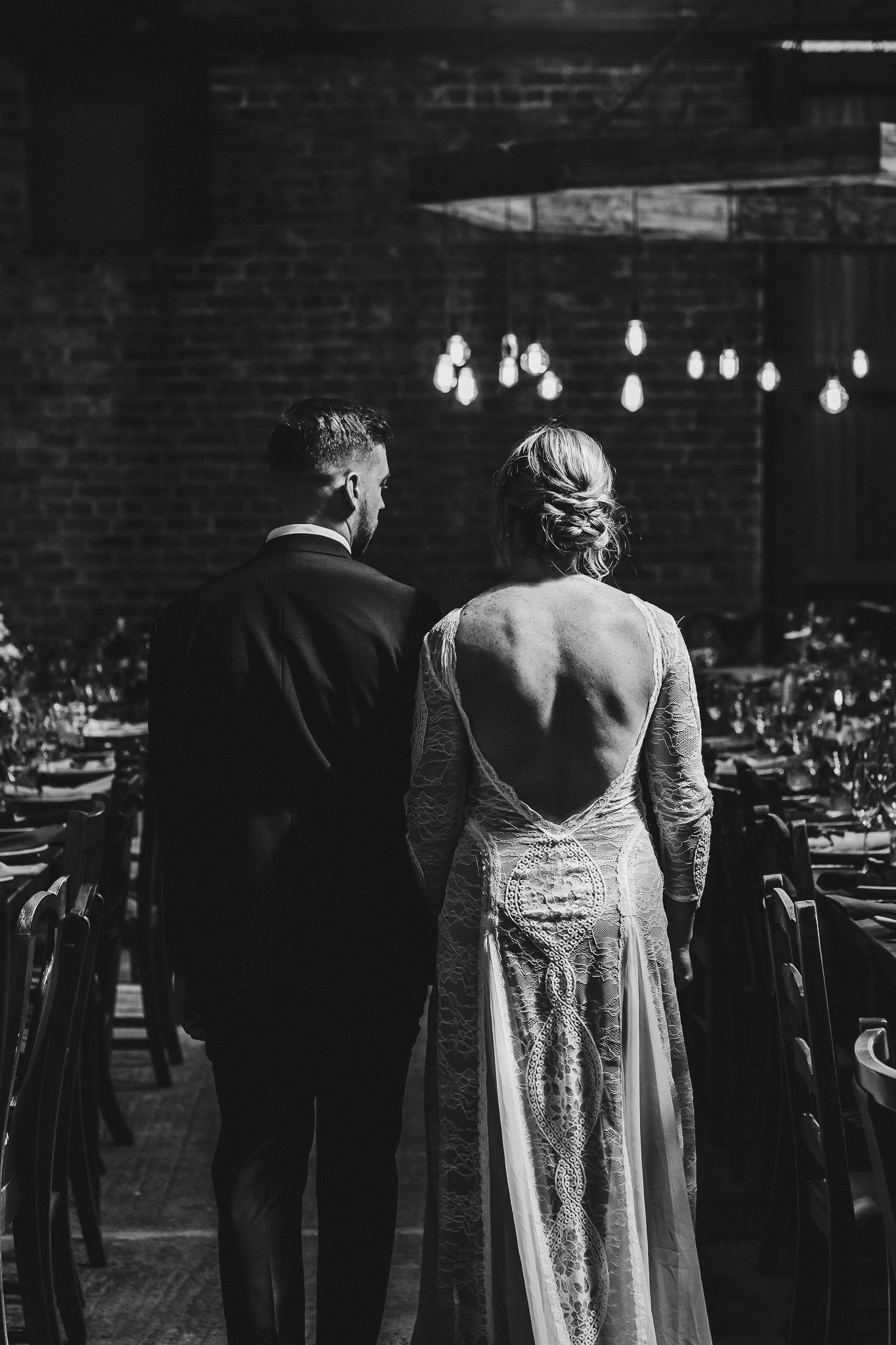 Black and white image of couple overlooking wedding reception tables in rustic venue.