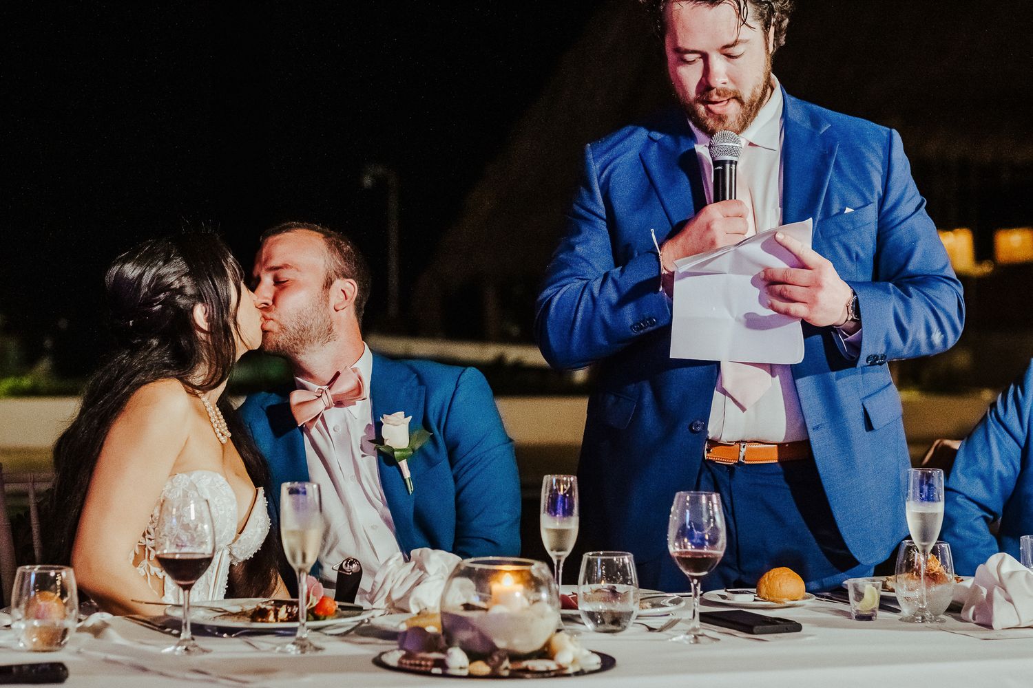 Wedding reception dinner with guests enjoying toasts and laughter at an outdoor venue.