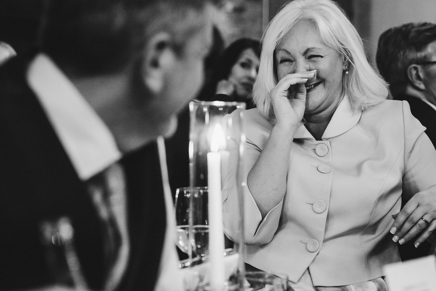 Black and white candid moment of guests laughing during formal dinner event.
