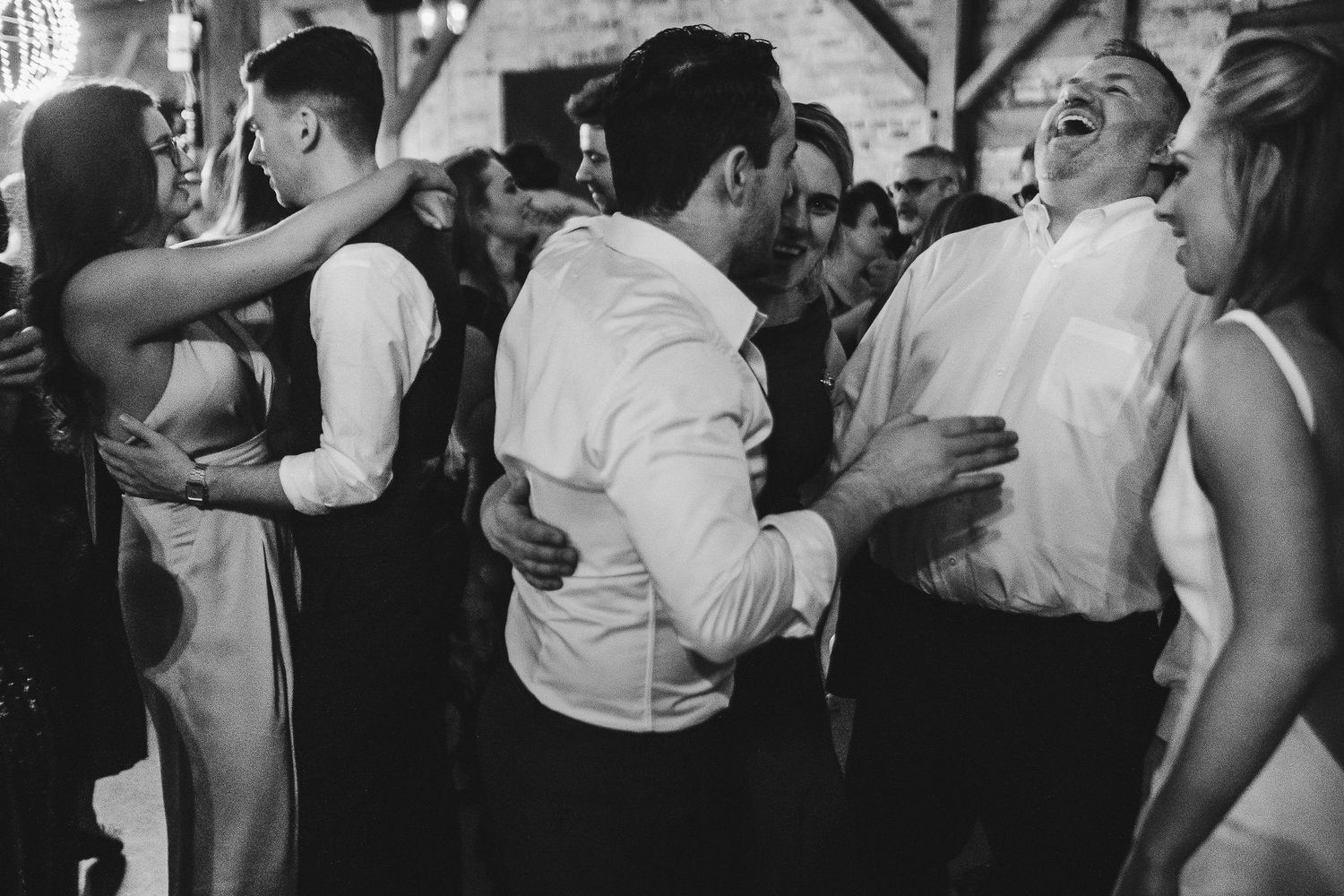 Black and white photo of wedding guests dancing close together at reception.