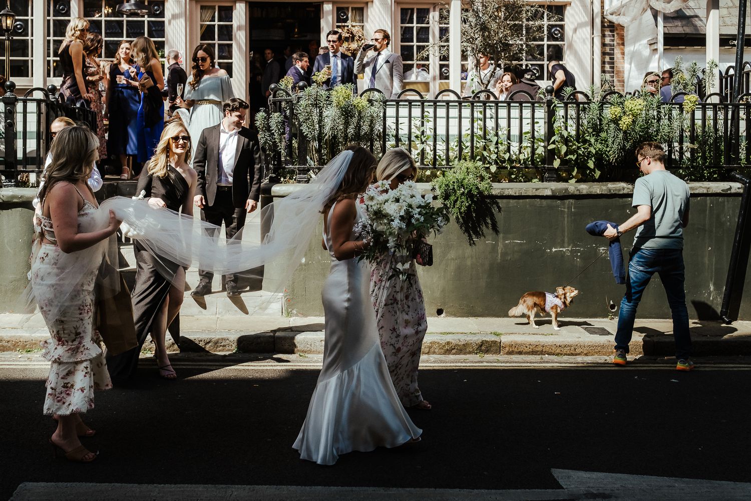 Wedding party gathers outside a historic building with street lamps and ornate architecture.