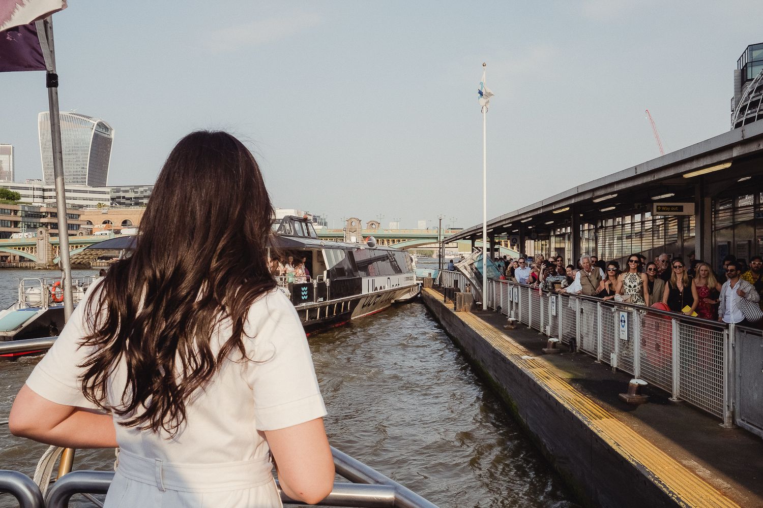 Passengers wait at a crowded boat terminal platform along Bangkok's Chao Phraya River on a hazy afternoon.
