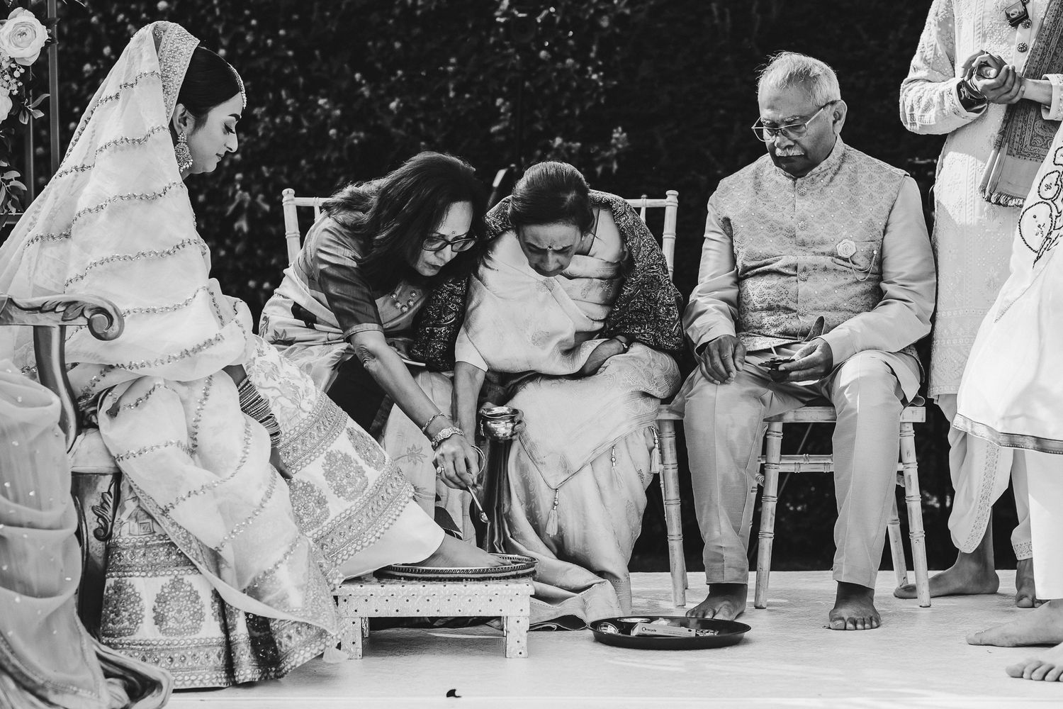 A vintage black and white photograph shows a small gathering of people seated outdoors in traditional Indian attire.