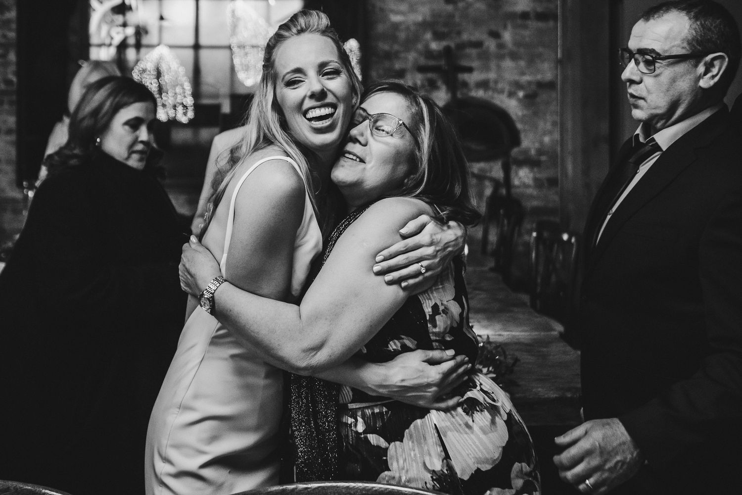 A heartfelt embrace shared between wedding guests at an indoor reception venue.