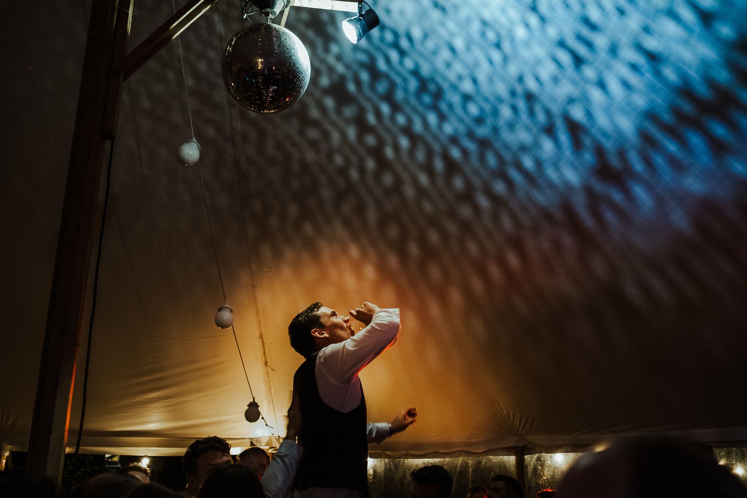 Blue lighting creates dramatic atmosphere under a wedding reception tent ceiling.