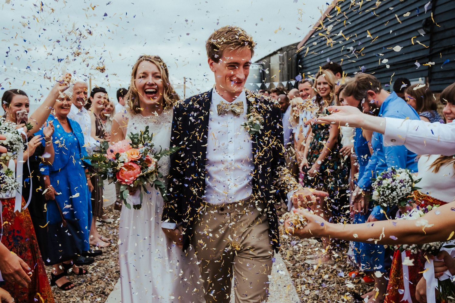 Confetti shower celebration with guests showering newlyweds with joyful enthusiasm outside a rustic venue.