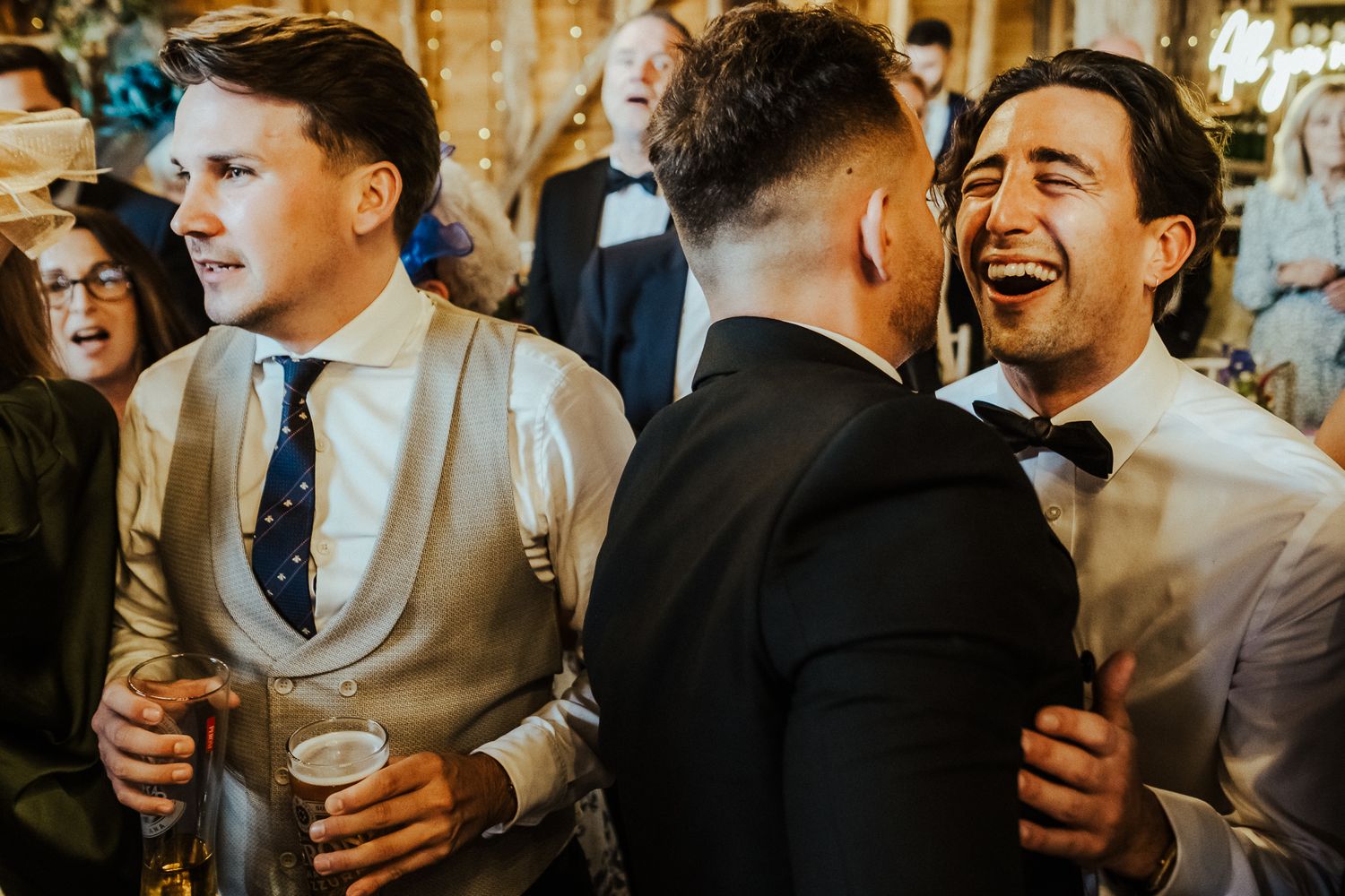 Wedding guests laughing and celebrating with drinks during the reception party.