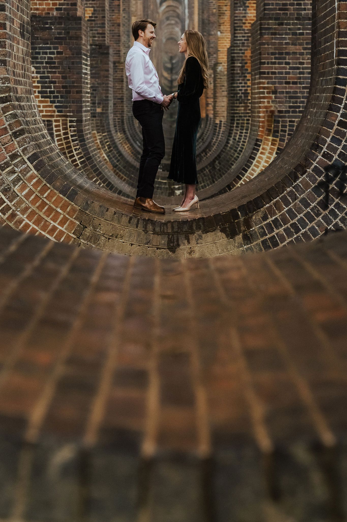 Couple standing in a dramatic curved brick archway creating a unique perspective shot.