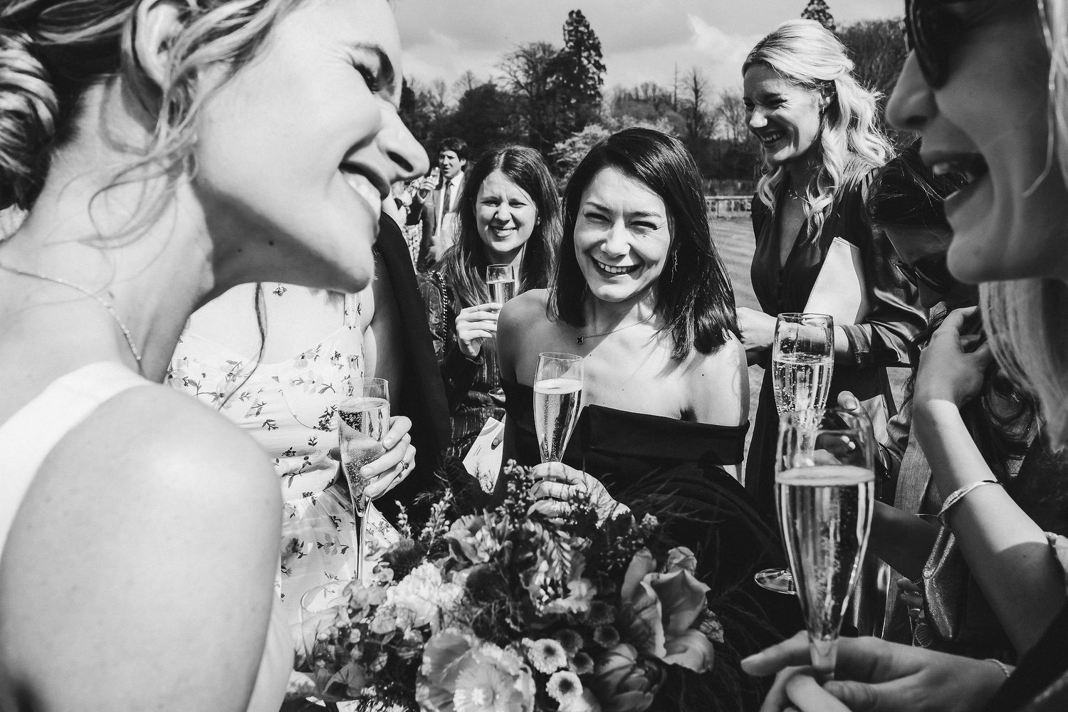 Black and white candid photo of wedding guests enjoying champagne and conversation.