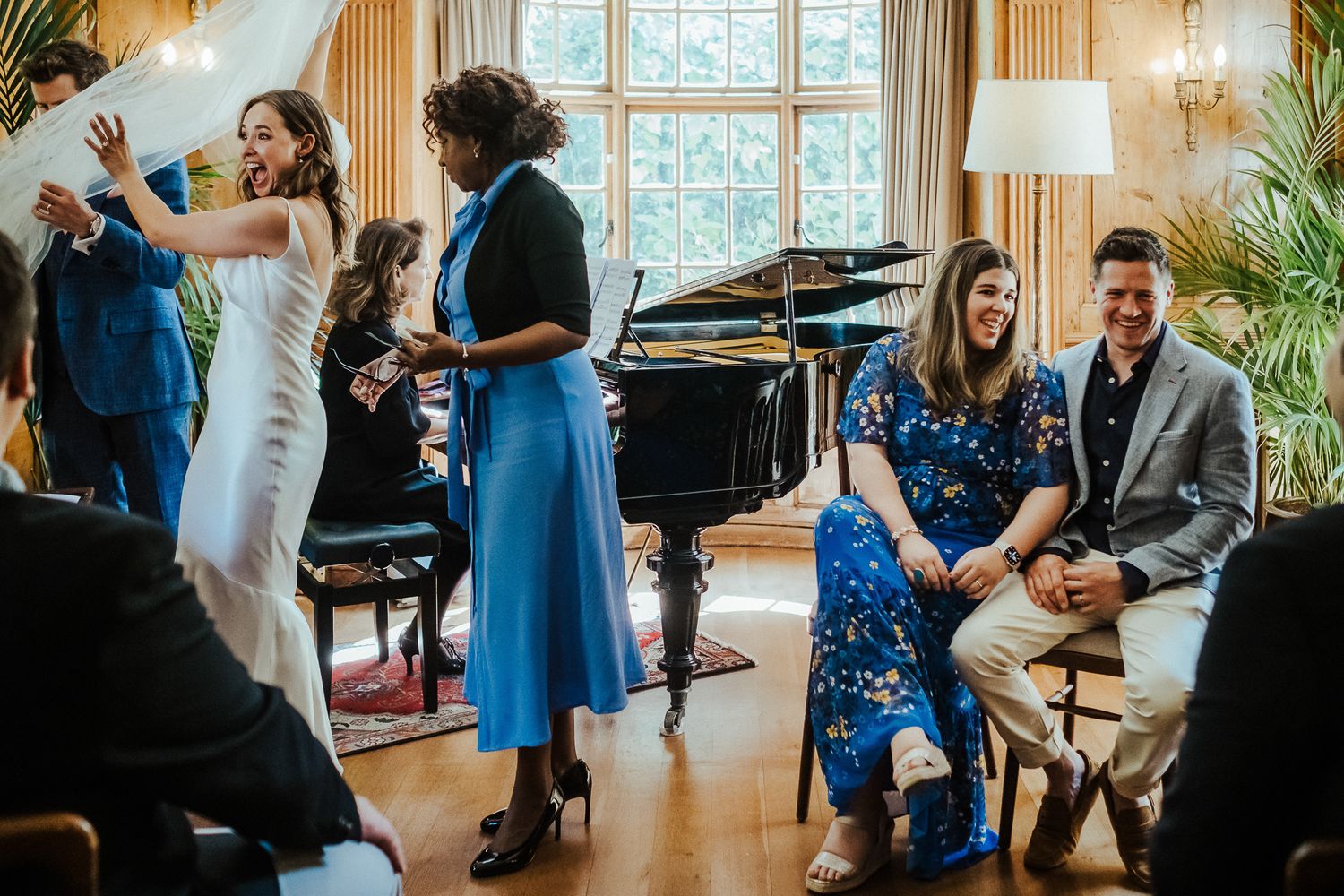 Wedding celebration in an elegant room with guests dancing and mingling near a grand piano.