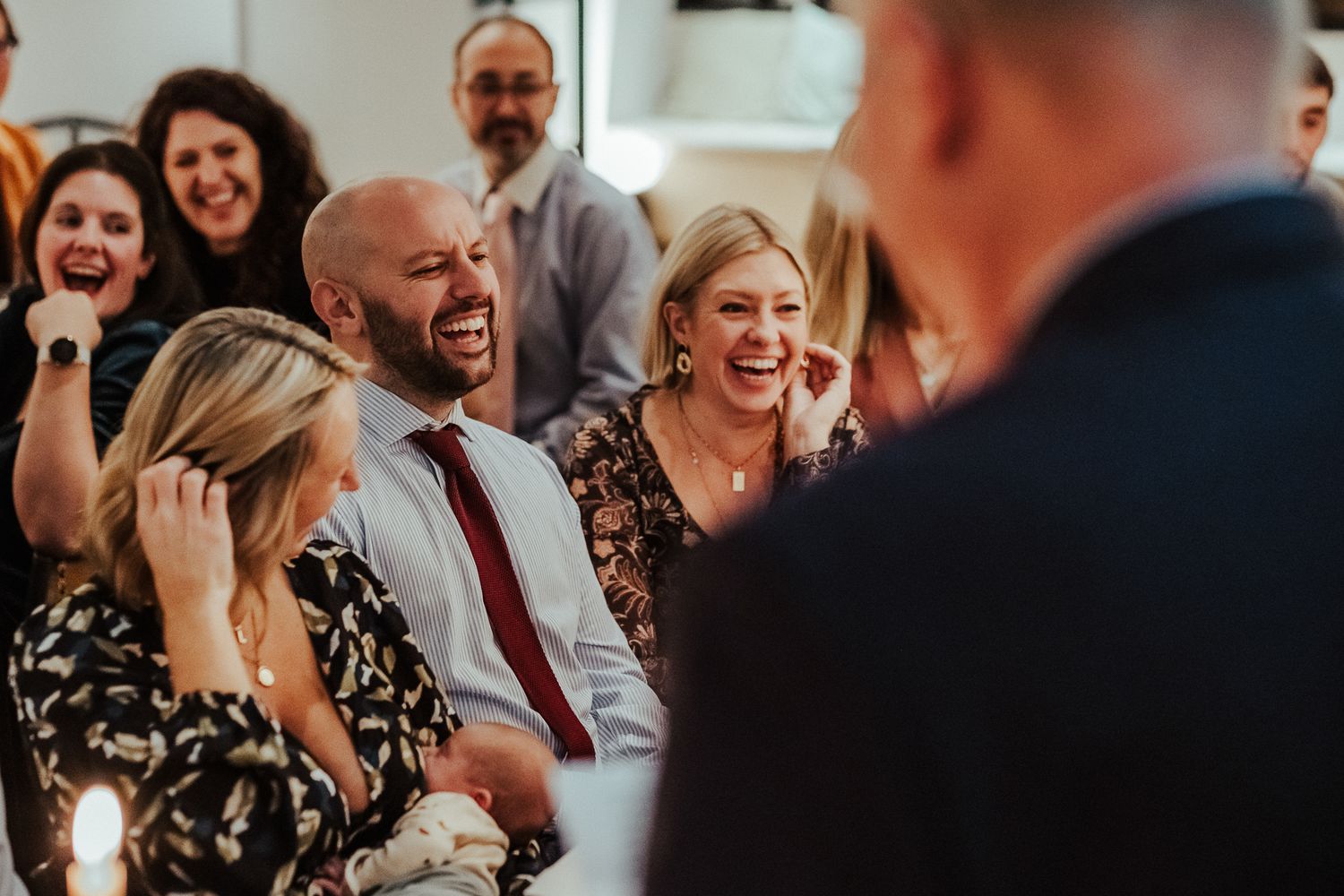 Wedding guests laugh and socialize during a warm reception gathering.