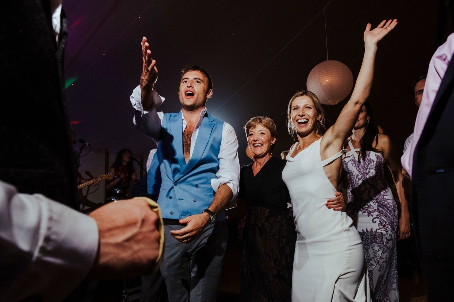 Wedding guests dance and celebrate energetically on a dark dance floor.