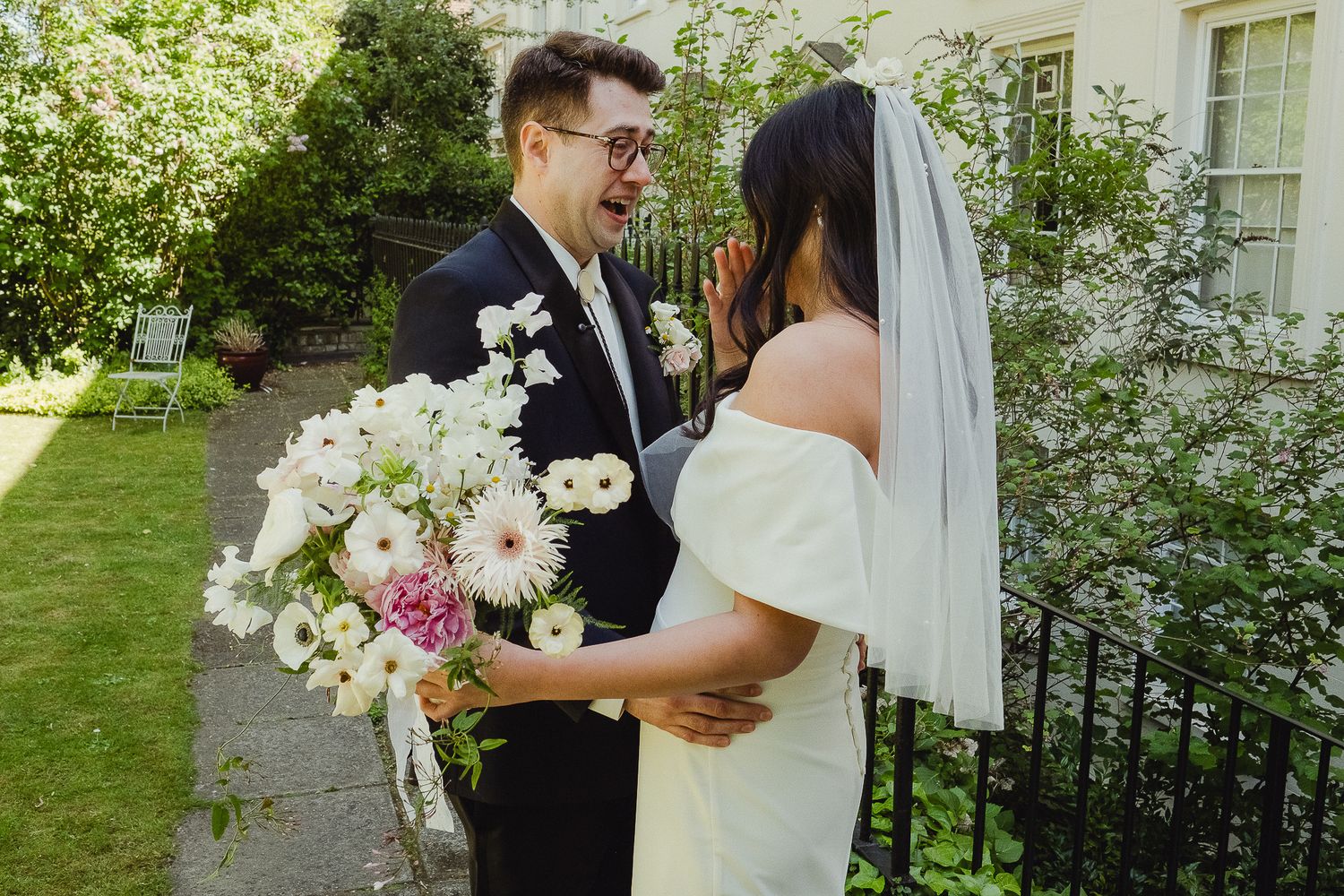 A lovely outdoor wedding scene with a smiling couple sharing a moment in a garden while holding a beautiful floral bouquet.