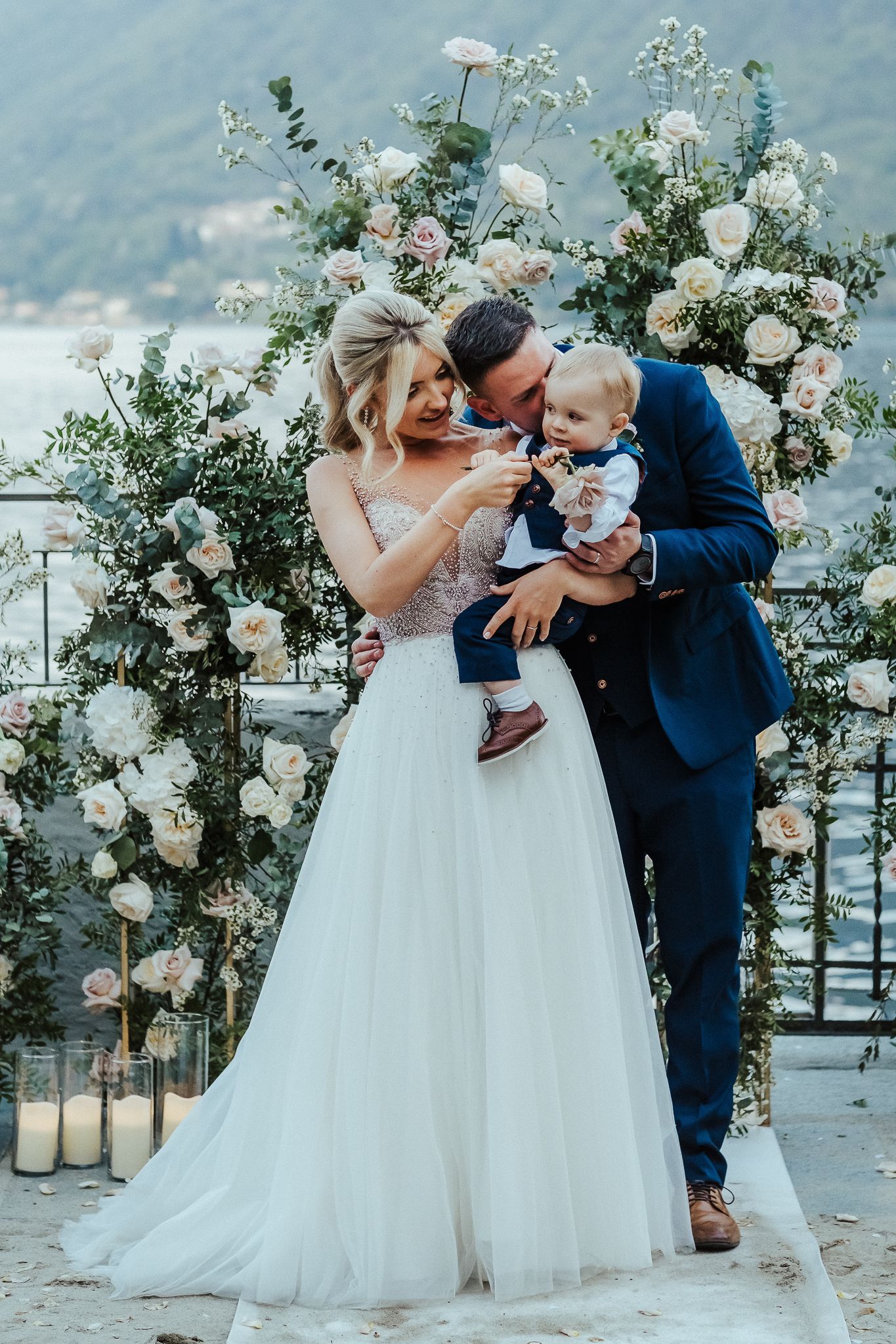 Beautiful wedding portrait with white floral arch overlooking a scenic lake view.