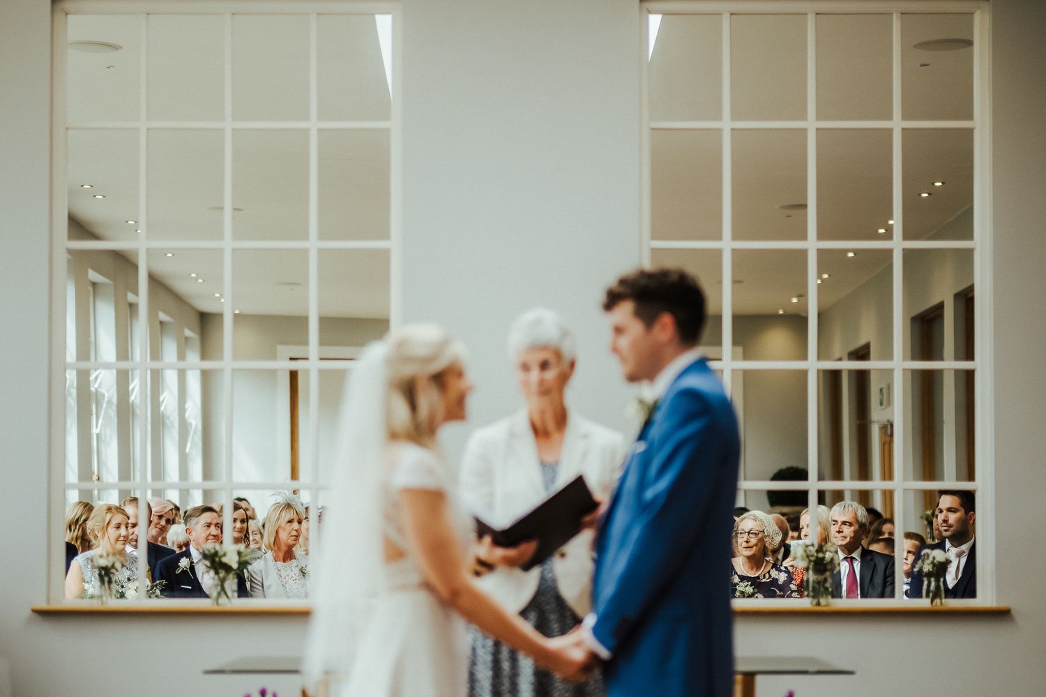 Intimate wedding ceremony in bright interior with windowed walls.