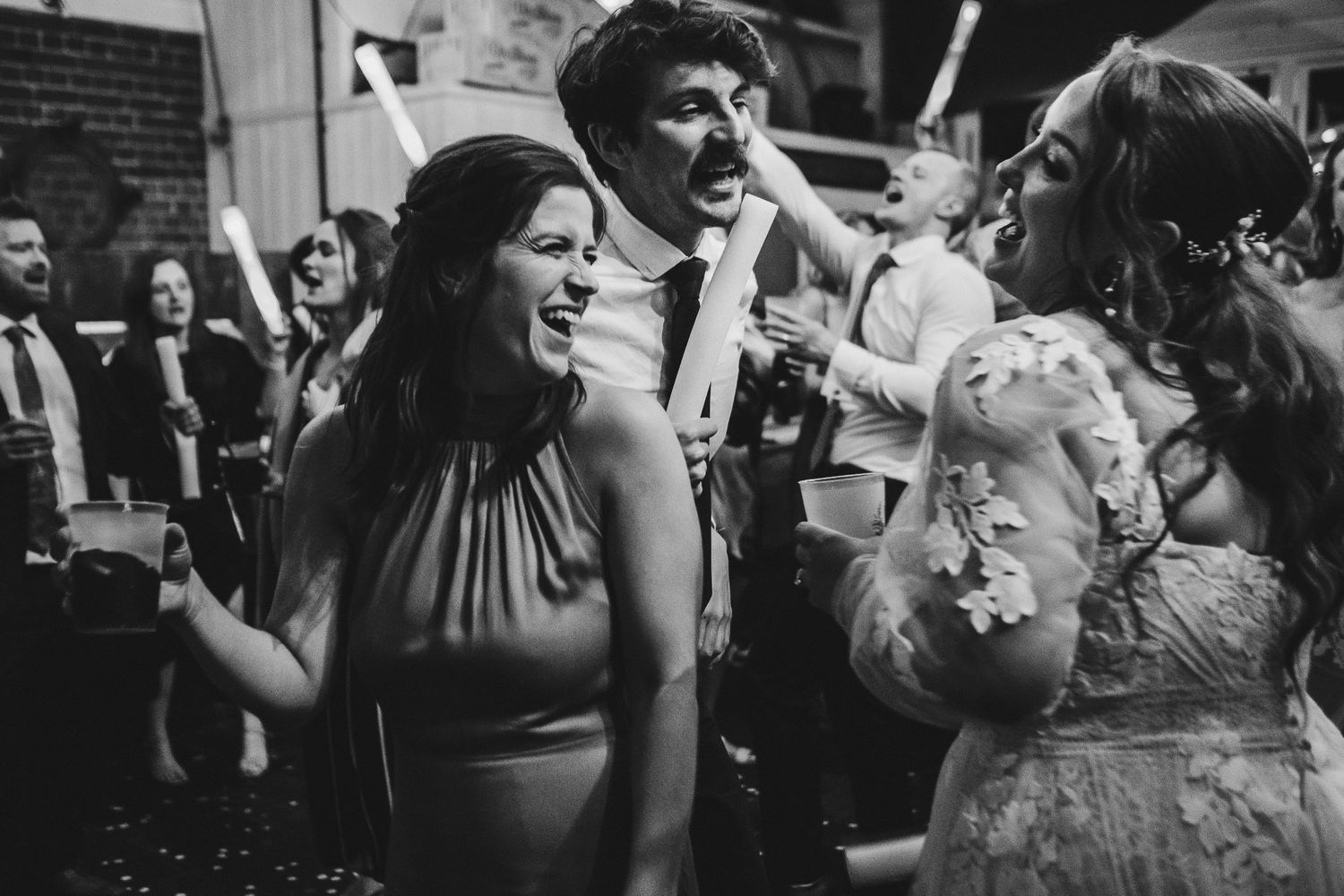 Joyful wedding guests dance and celebrate with glowing batons at a reception.