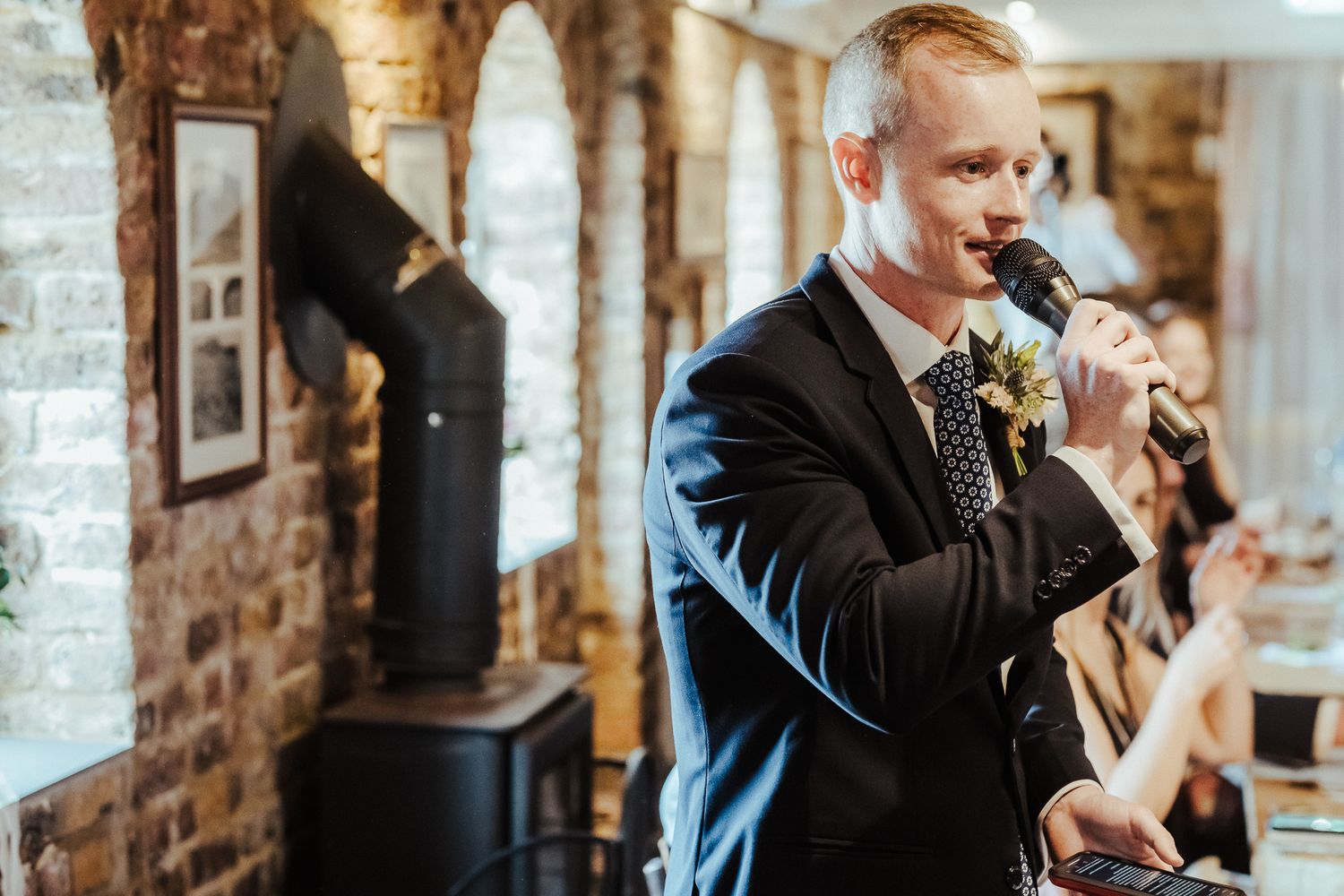 Groom giving emotional wedding speech in rustic brick venue.