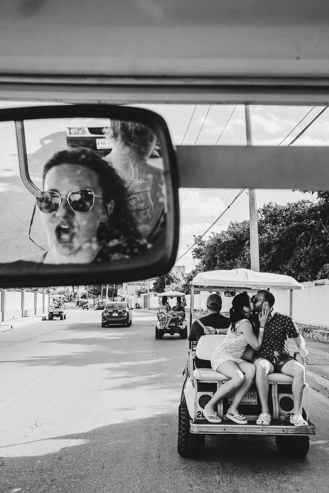 Black and white photo of golf carts driving with side mirror reflection.