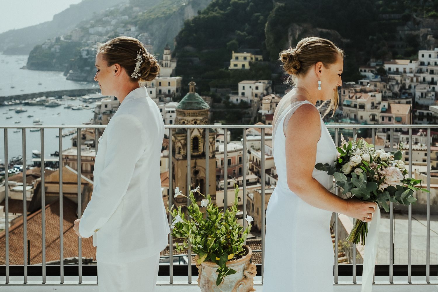 Two people in white dresses walk along a scenic terrace in Positano, Italy.