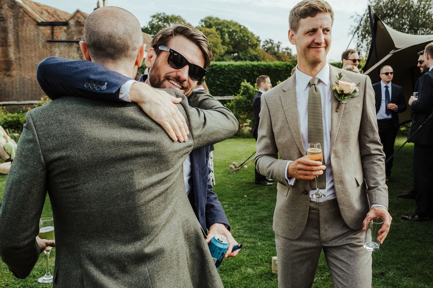 Men in suits embrace during casual outdoor wedding reception.