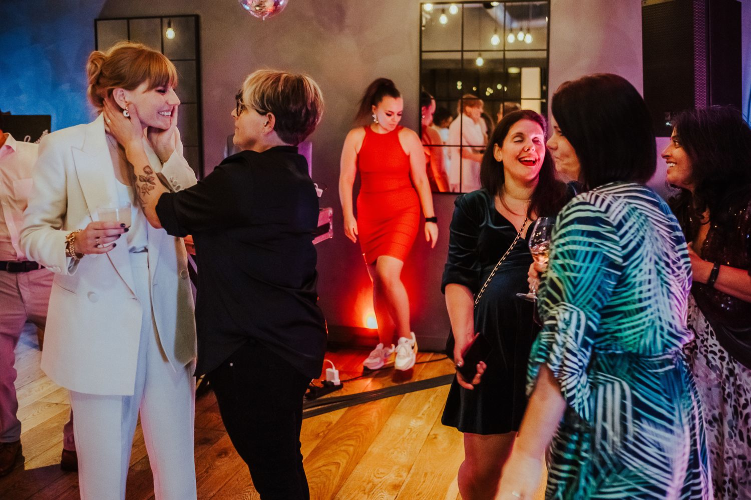 People socializing and dancing at a festive indoor party with pink lighting.