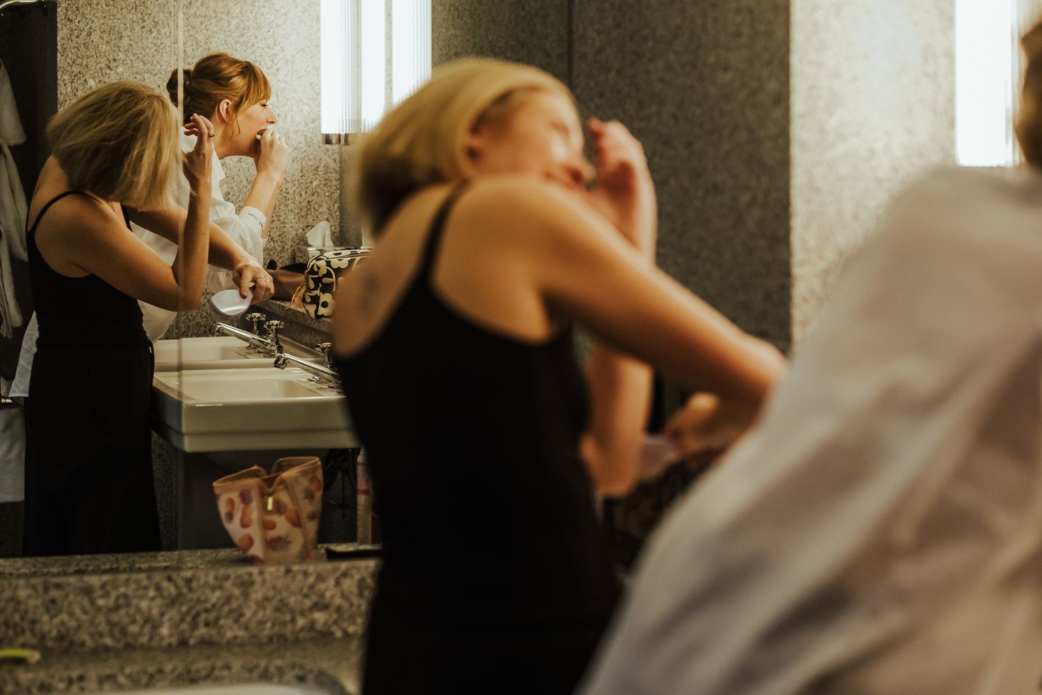 Wedding party getting ready in a bathroom with mirrors and decorative lighting.