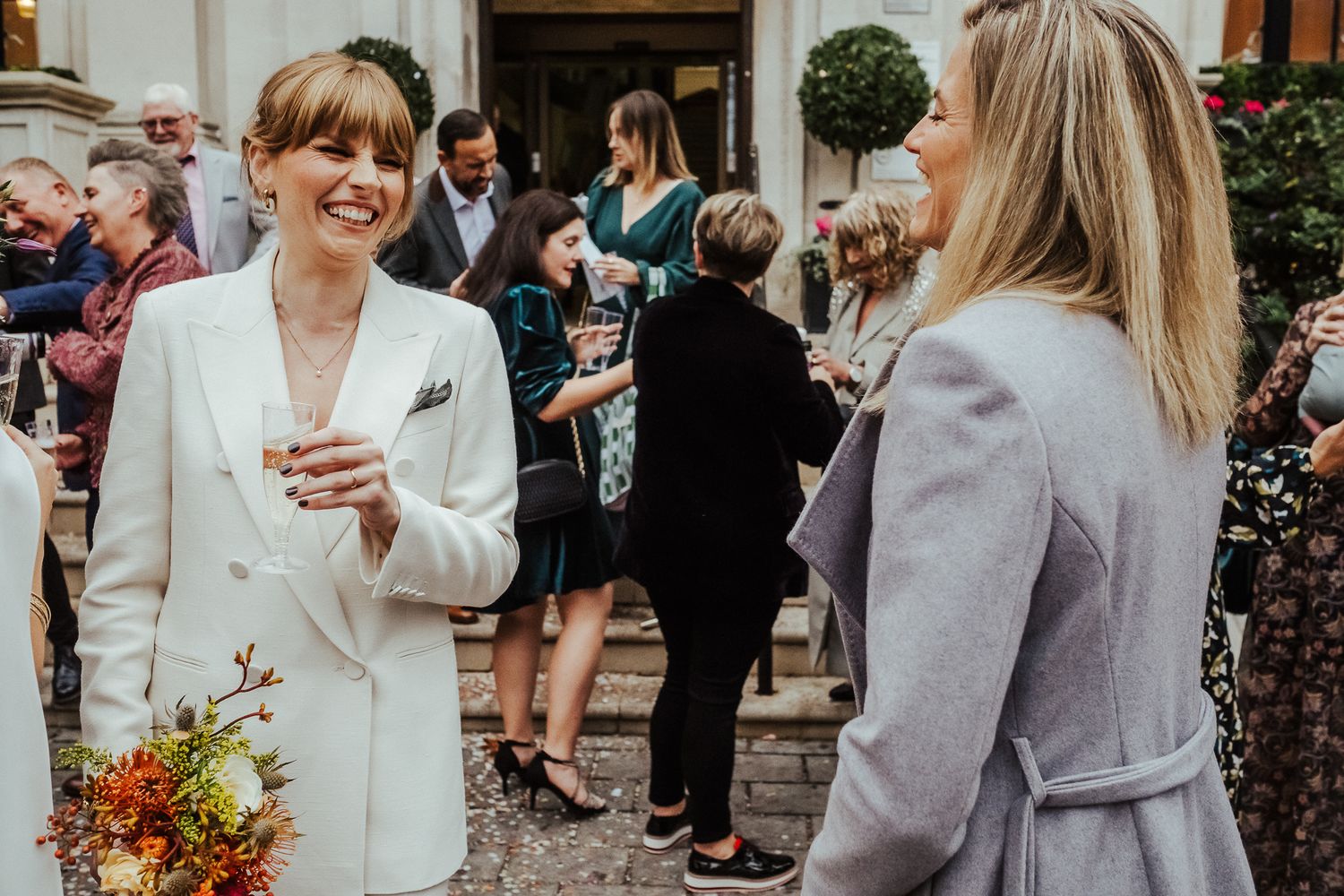 Wedding guests mingle and celebrate outside a classic building entrance.