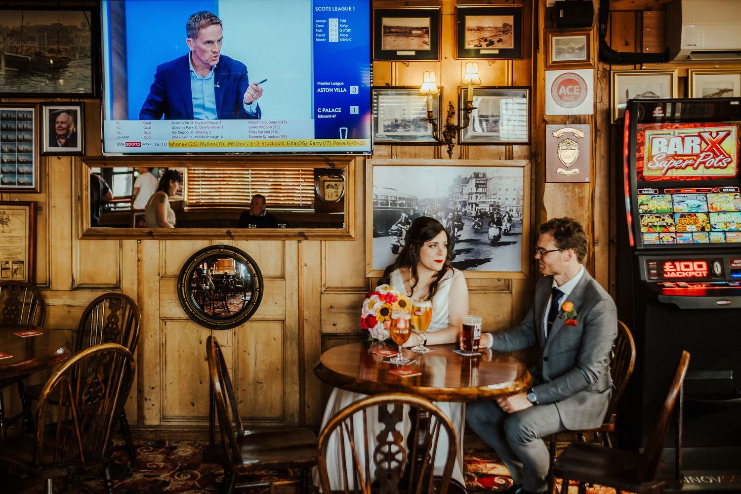 Couple sharing intimate moment at pub table with TV screen in background.