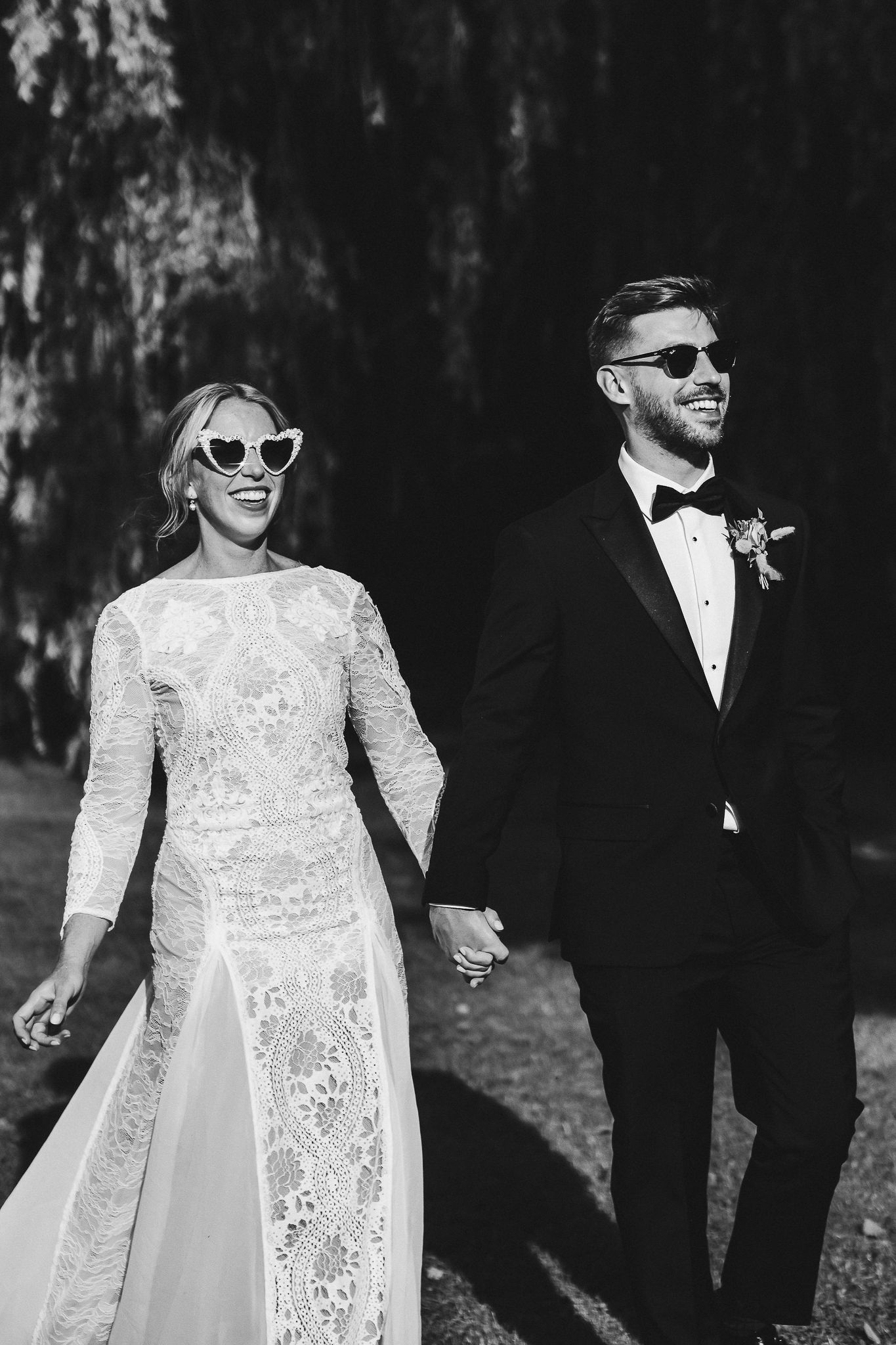 Black and white photo of stylish wedding couple wearing sunglasses and walking together.