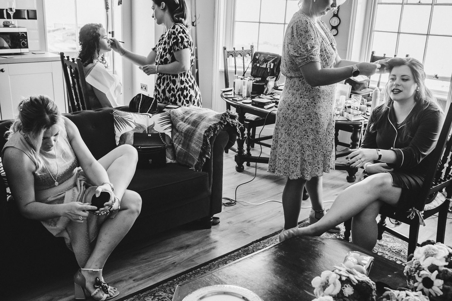 A black and white photo captures wedding party preparations in a cozy living room setting.