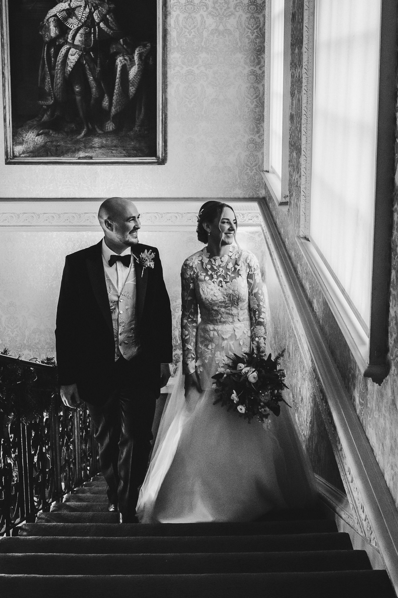 Black and white wedding portrait on grand staircase with vintage artwork.