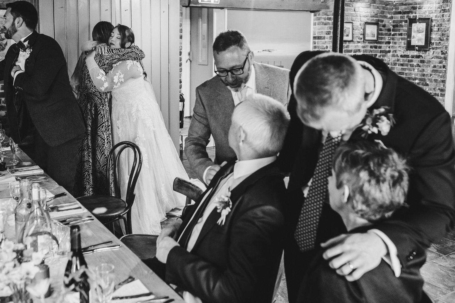 Black and white candid photo of wedding reception guests sharing emotional moments.