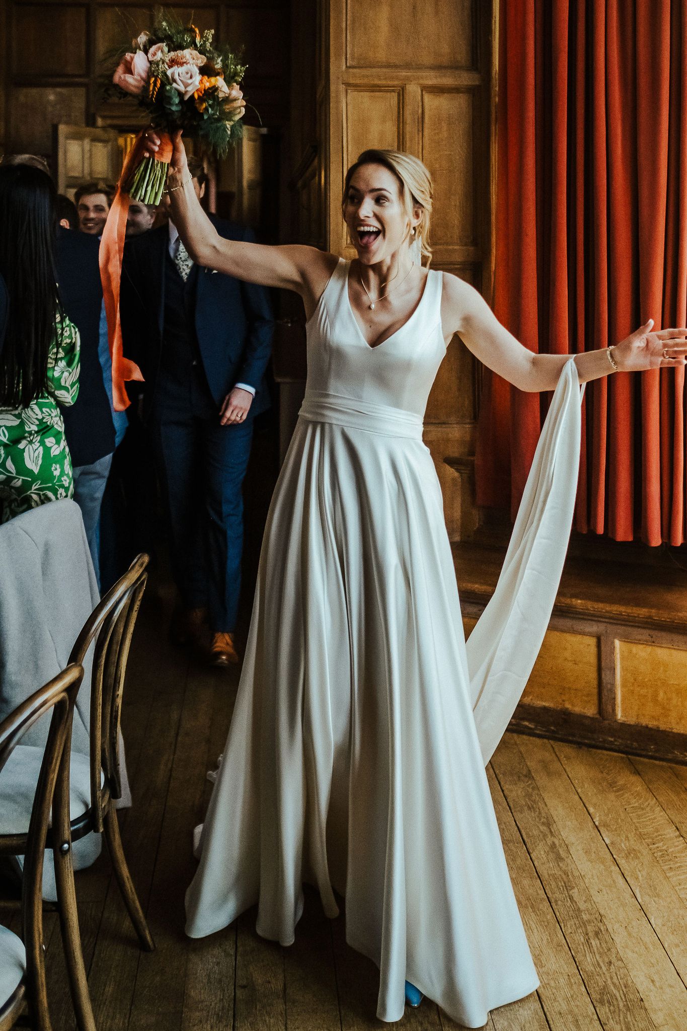 Joyful celebration in a rustic wooden venue with elegant white wedding dress and orange curtains.