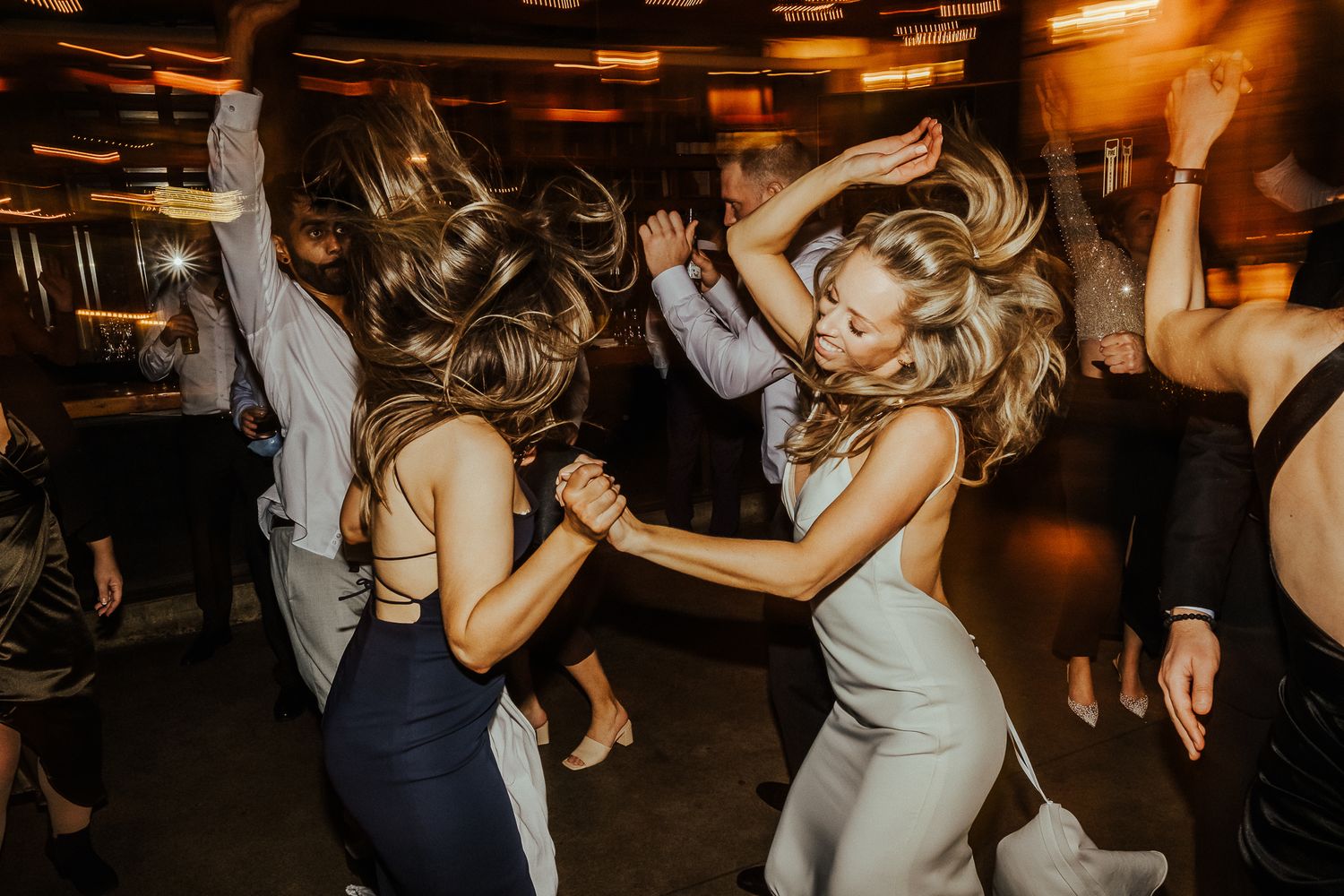 Wedding guests dancing enthusiastically at a dimly lit reception party.