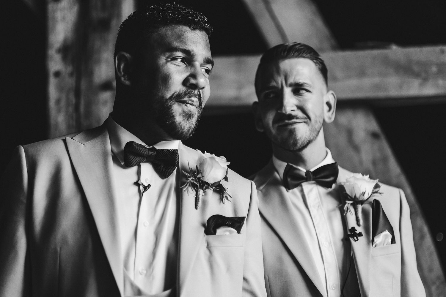 Two grooms in matching light colored tuxedos share intimate black and white portrait.
