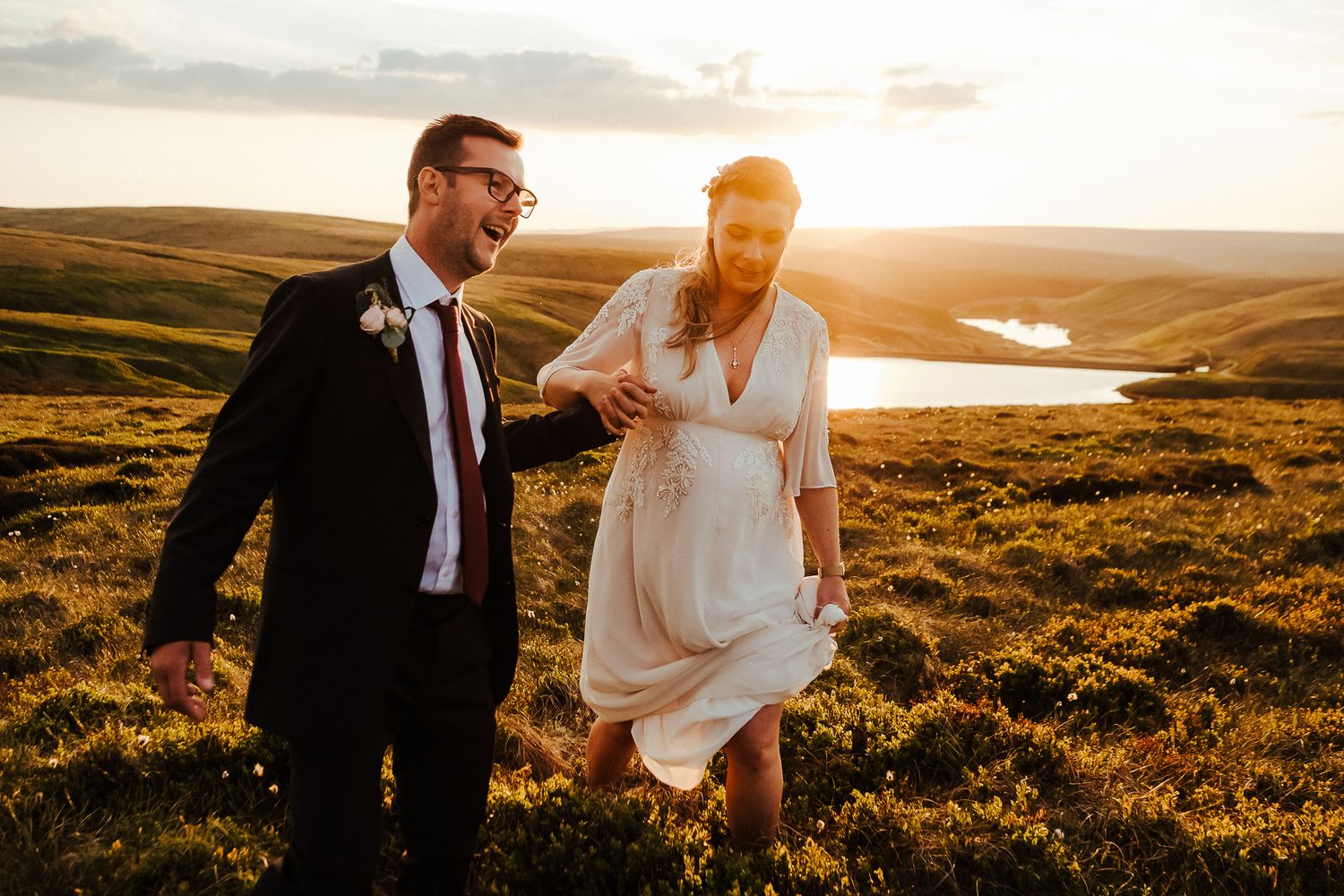 Wedding couple embraces in golden sunset light on rolling hills with dramatic sky.