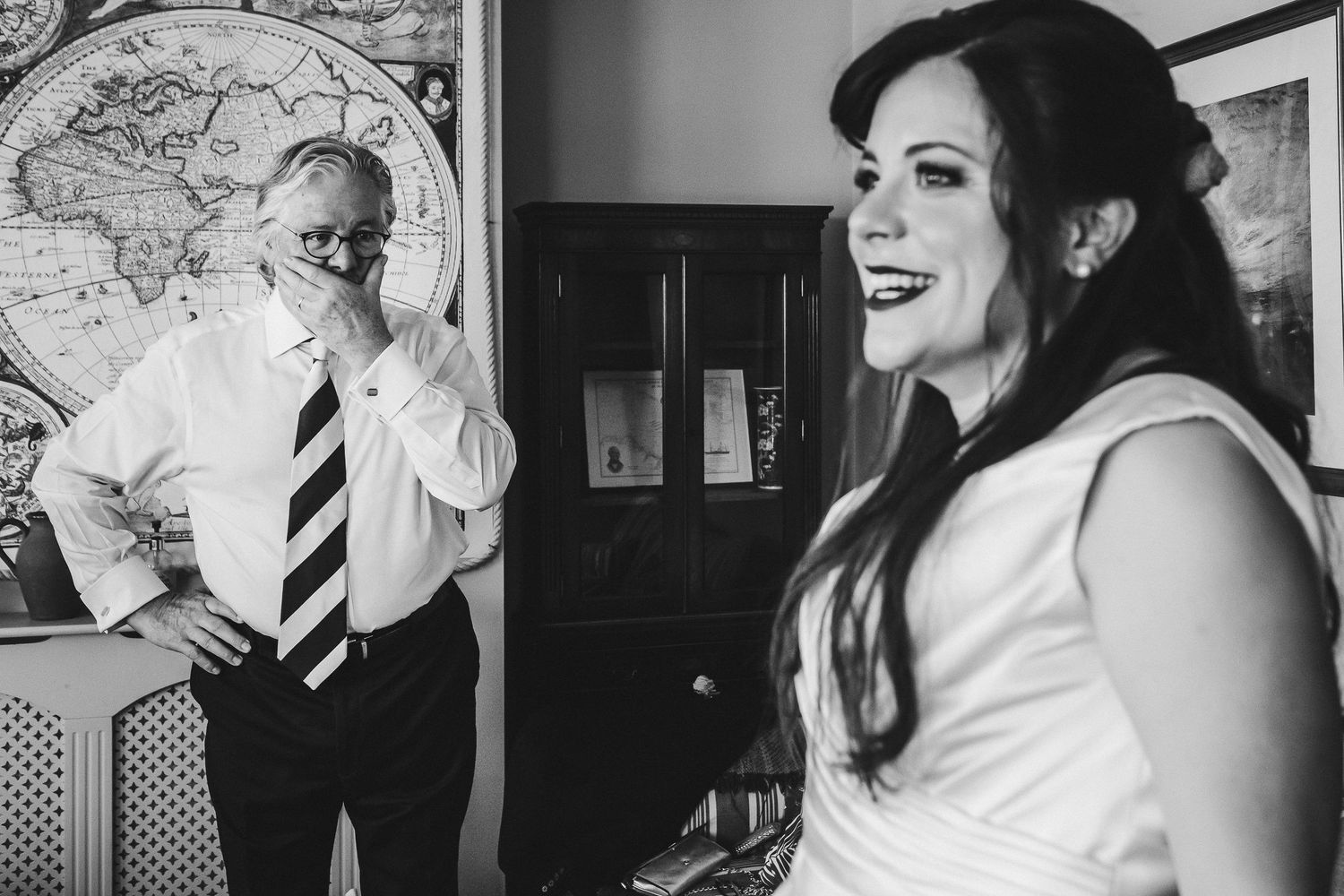 Black and white wedding photo with world map backdrop showing joyful pre-ceremony moment.