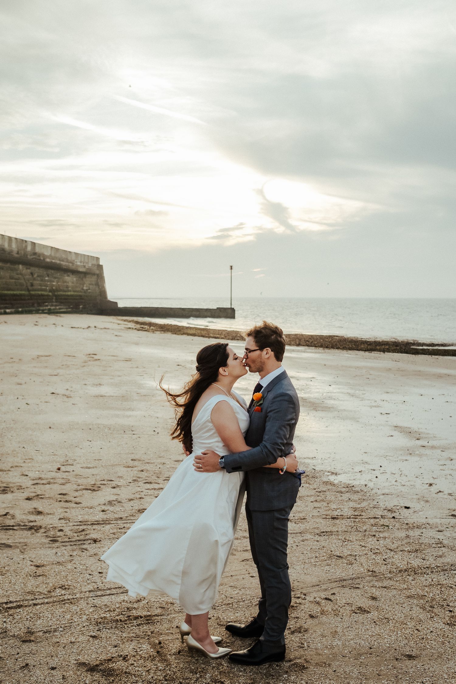 Romantic sunset beach portrait with couple embracing against cloudy sky.