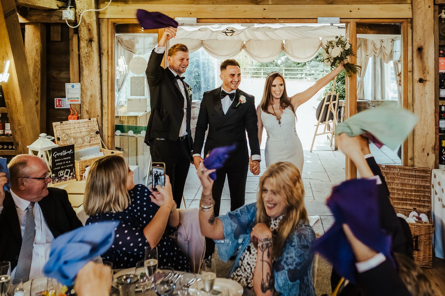 Wedding guests celebrate during a reception in a rustic wooden venue.