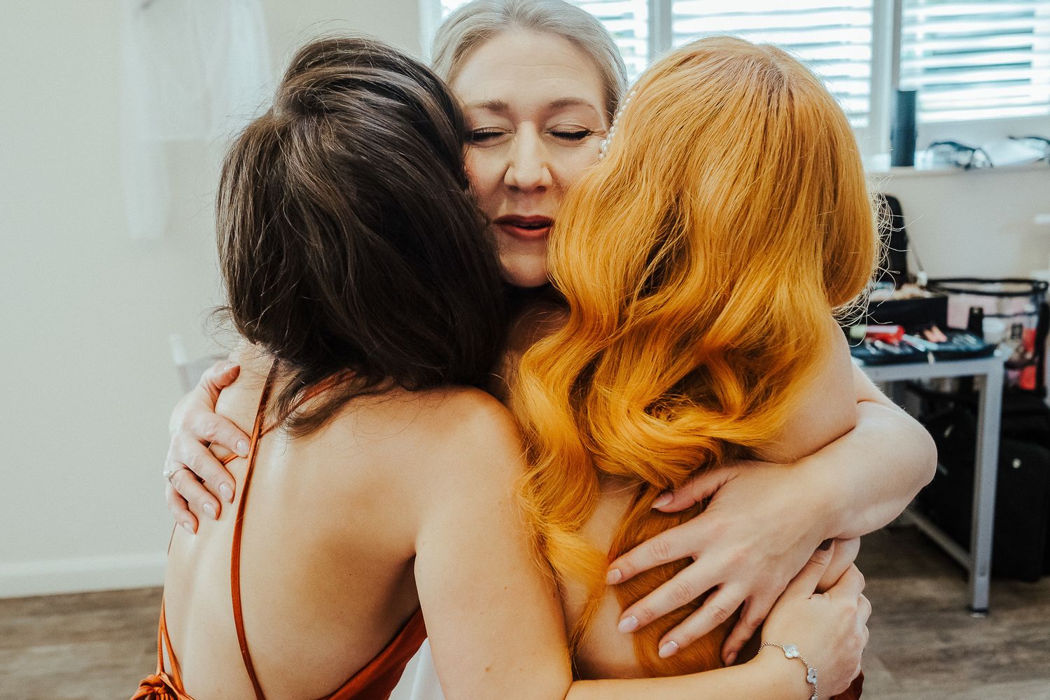 Three people share an emotional embrace in an indoor setting.