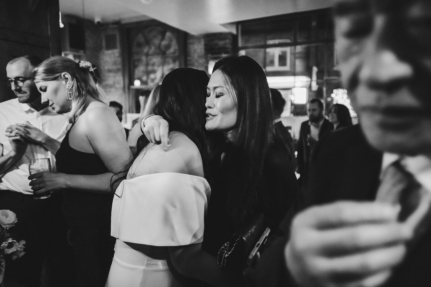 Black and white photo showing people gathered in a crowded bar or restaurant with patrons engaged in lively conversation.